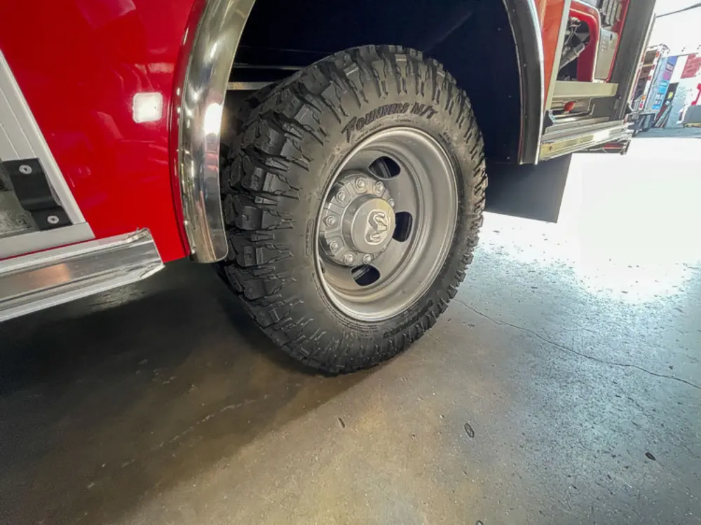 Exterior view of small fire truck showing cab, body compartments, and wheel/tire area.
